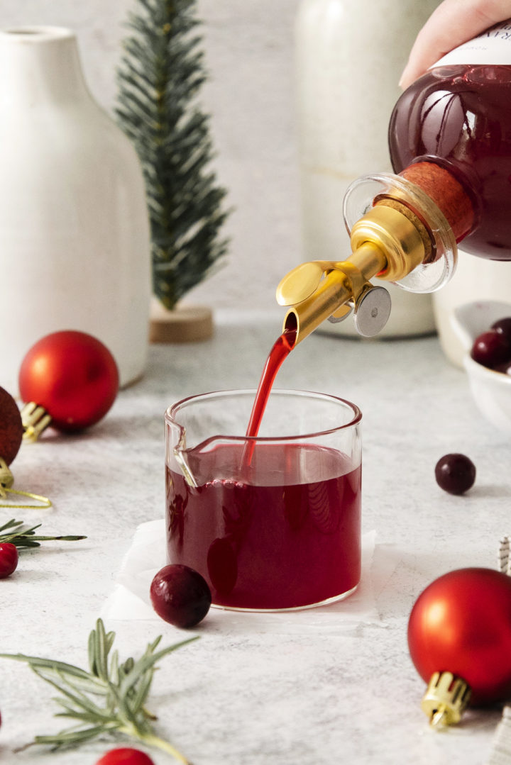 pouring cranberry simple syrup into a measuring glass