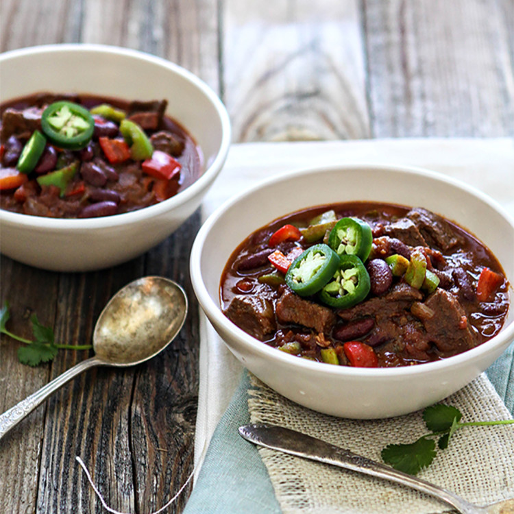 two bowls of short rib chili on a wooden table