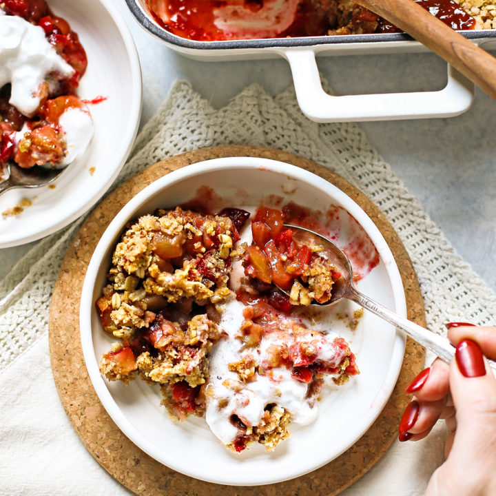 woman eating apple cranberry crisp from a white bowl