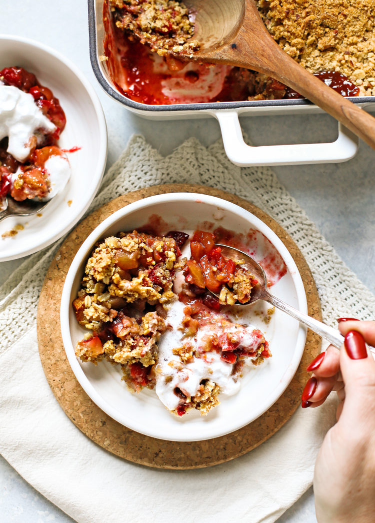 woman eating apple cranberry crisp from a white bowl