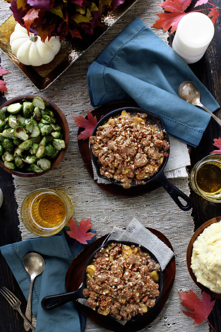 Overhead view of two mini cast iron skillets full of bourbon apple crisp, surrounded by fall table decor. 