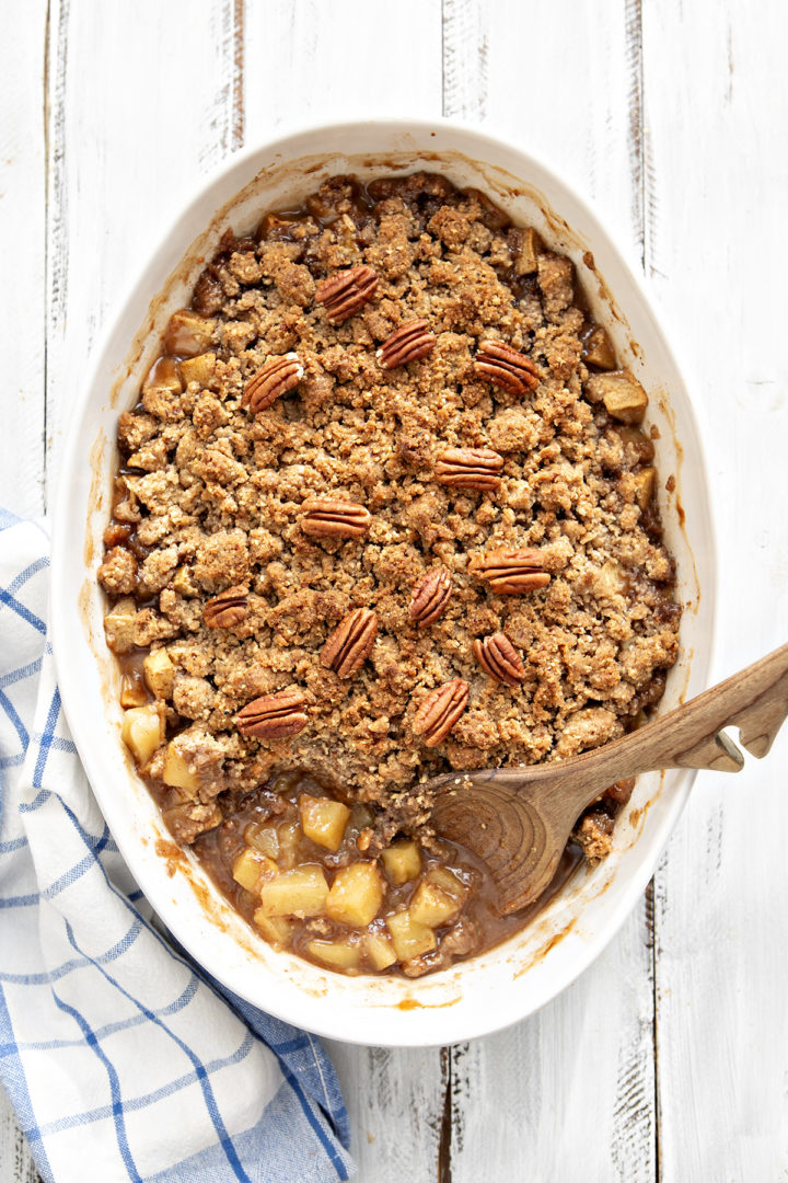 homemade apple crisp with oatmeal crumble topping in white baking dish with wooden spoon