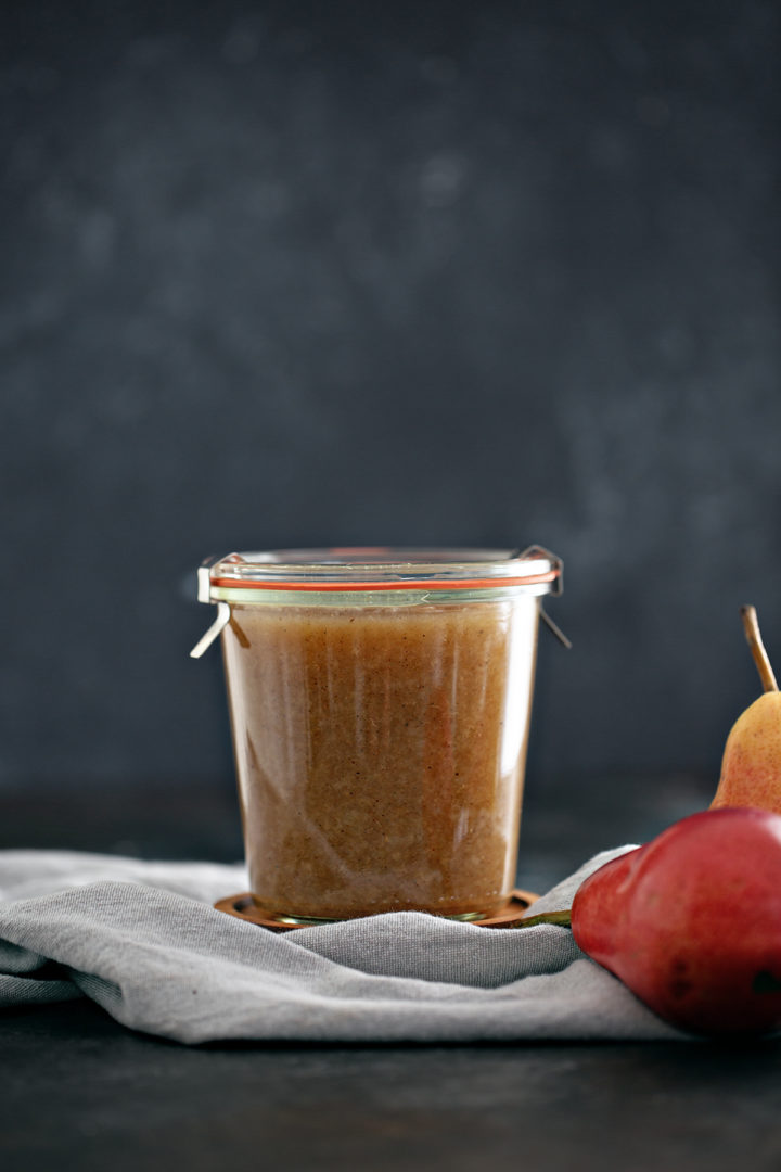 jar of canned pear sauce next to fresh pears on a dark background 