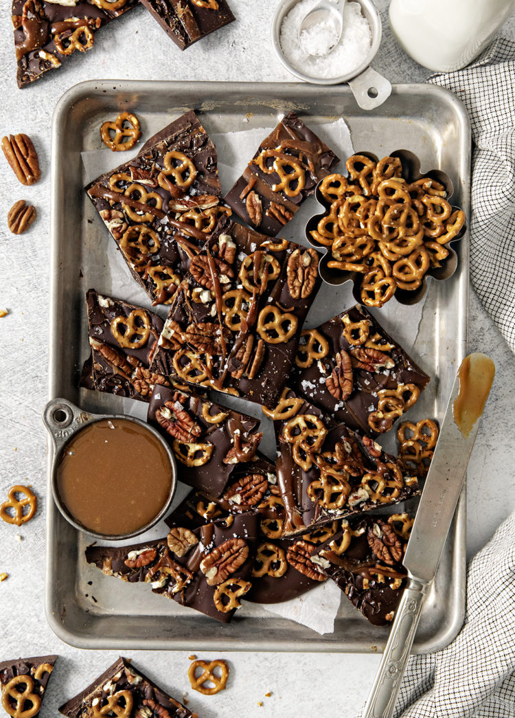 overhead photo of pretzel bark on a baking sheet next to a bowl of salted caramel