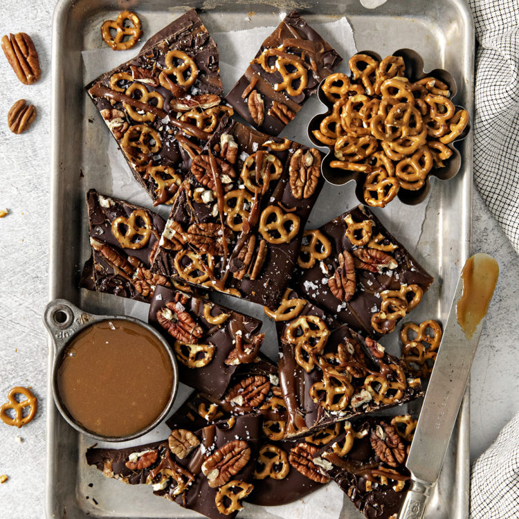 overhead photo of pretzel bark on a baking sheet next to a bowl of salted caramel