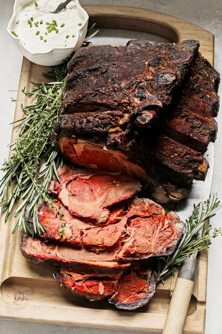 slices of Traeger prime rib roast on a wooden cutting board with fresh herbs and knife