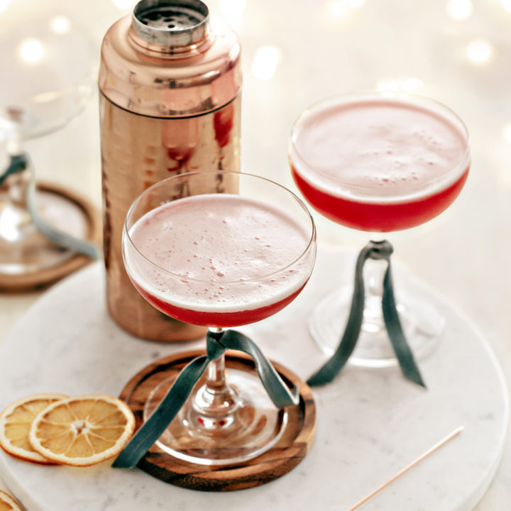 two coupe glasses filled with cranberry orange whiskey sour