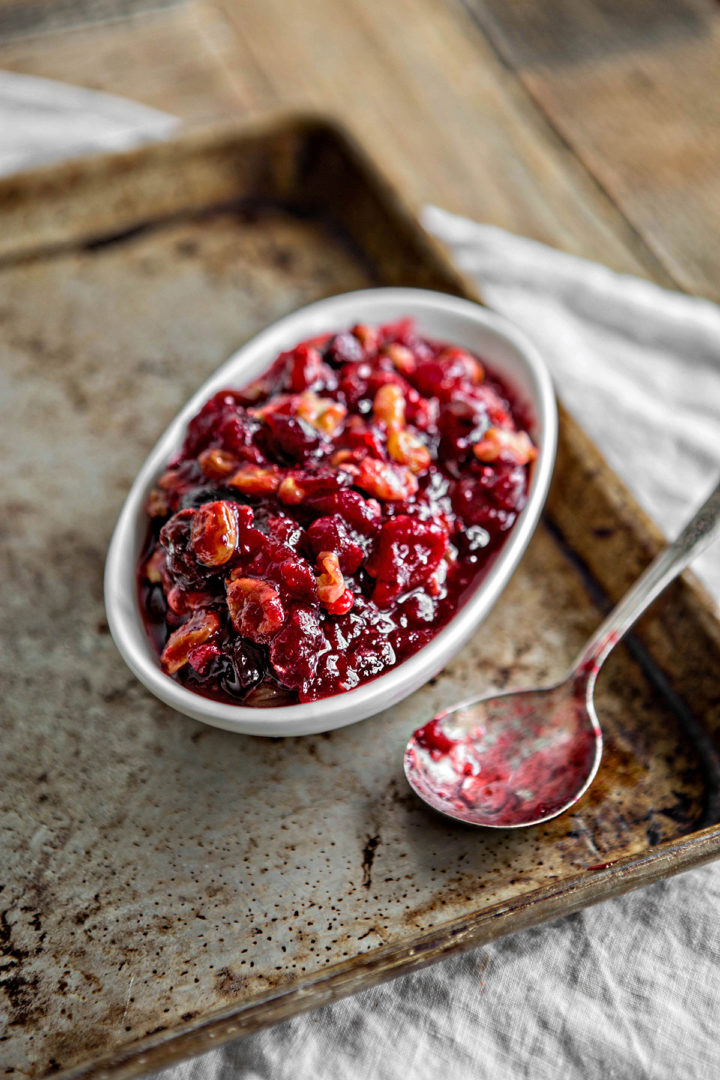 cranberry orange relish in white serving dish on baking tray next to spoon