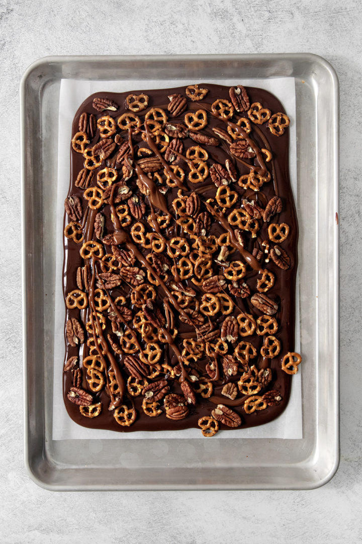 photo showing how to add the caramel, pecans, and pretzels on top of the dark chocolate to assemble the pretzel bark