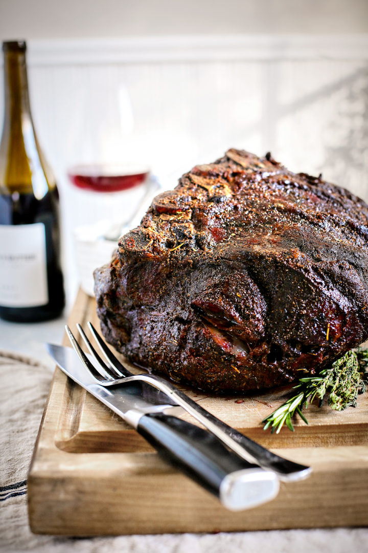 smoked prime rib resting on a cutting board with a fork and knife