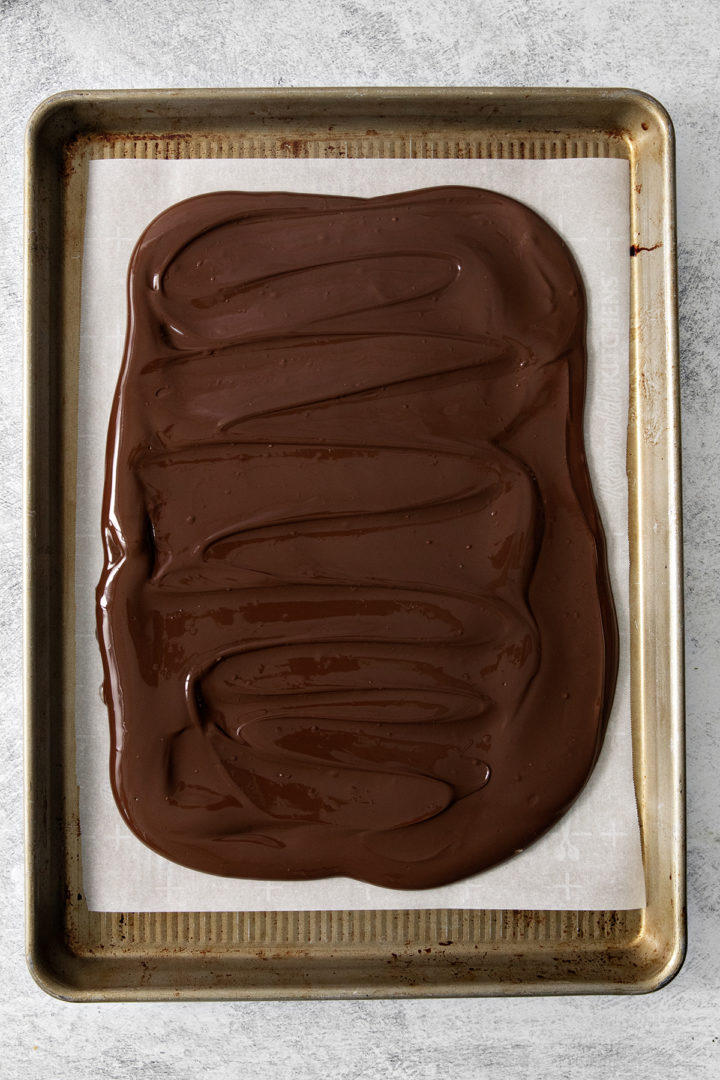 dark chocolate spread on a parchment paper lined sheet pan to make dark chocolate peppermint bark
