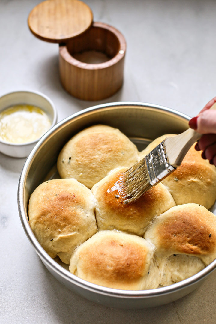 woman brushing melted butter on potato dinner rolls