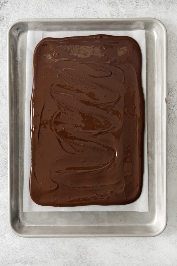 tempered dark chocolate spread on a parchment paper lined baking sheet for pretzel bark