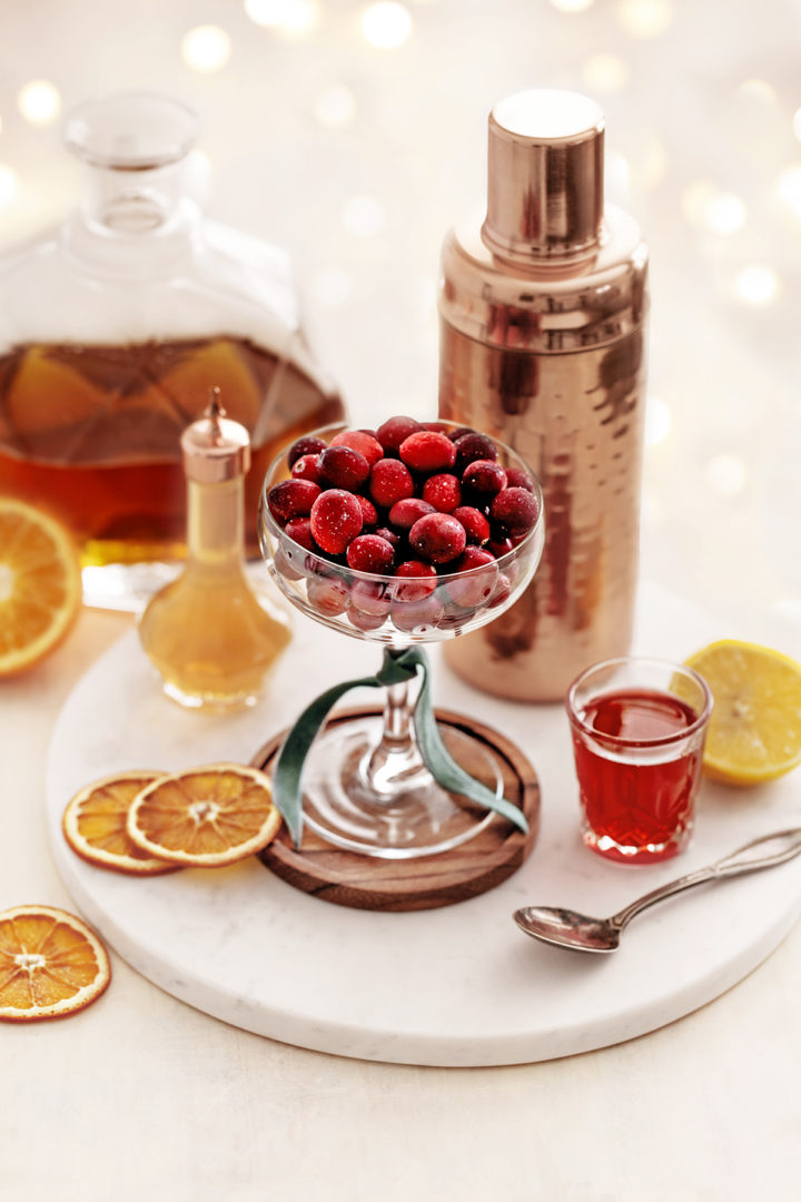 ingredients needed to make a cranberry orange whiskey sour on a marble tray with white lights in the background
