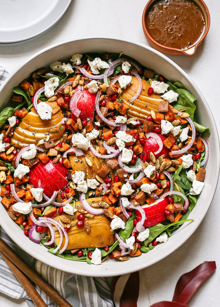 overhead photo of a pear and arugula salad for fall in a salad bowl next to a serving container of maple balsamic dressing