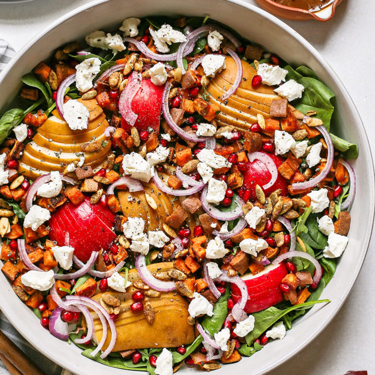 overhead photo of a pear and arugula salad for fall in a salad bowl next to a serving container of maple balsamic dressing