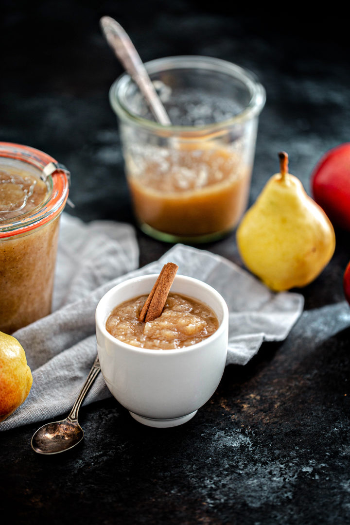 a bowl of pear sauce next to two jars