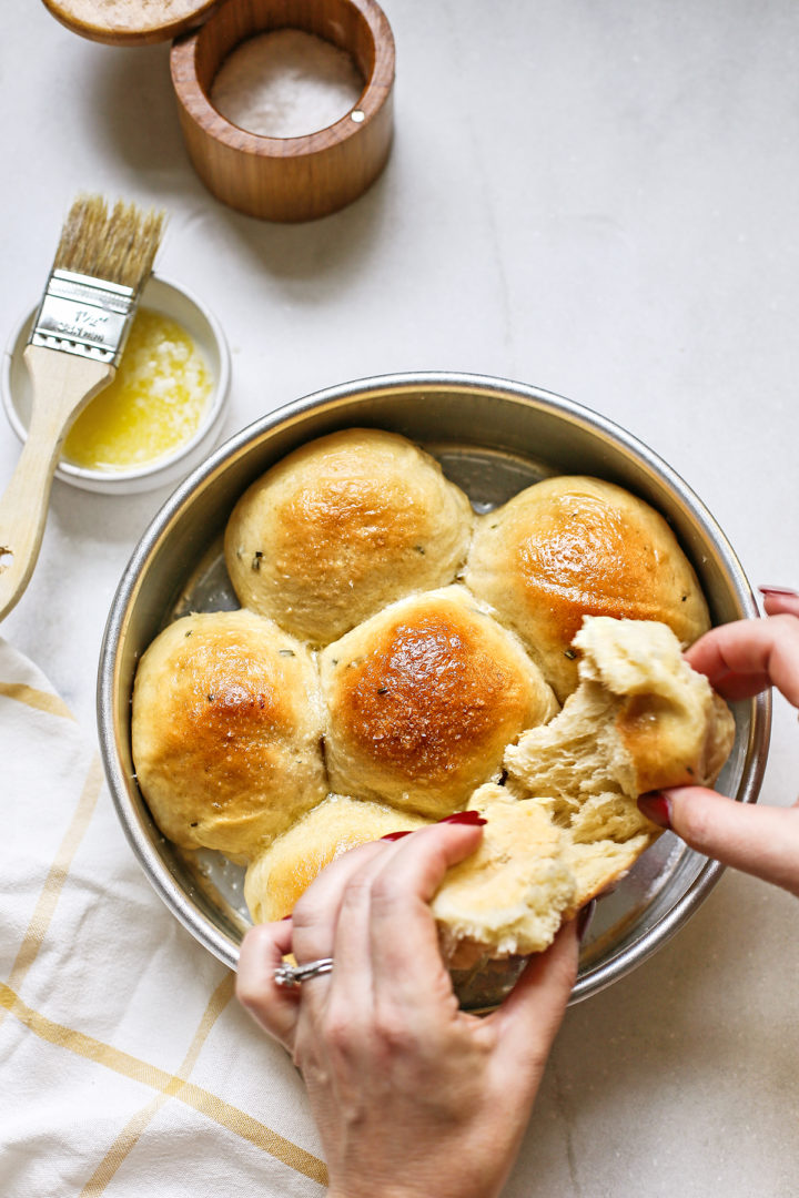 woman holding a potato roll next to a pan of fluffy potato dinner rolls