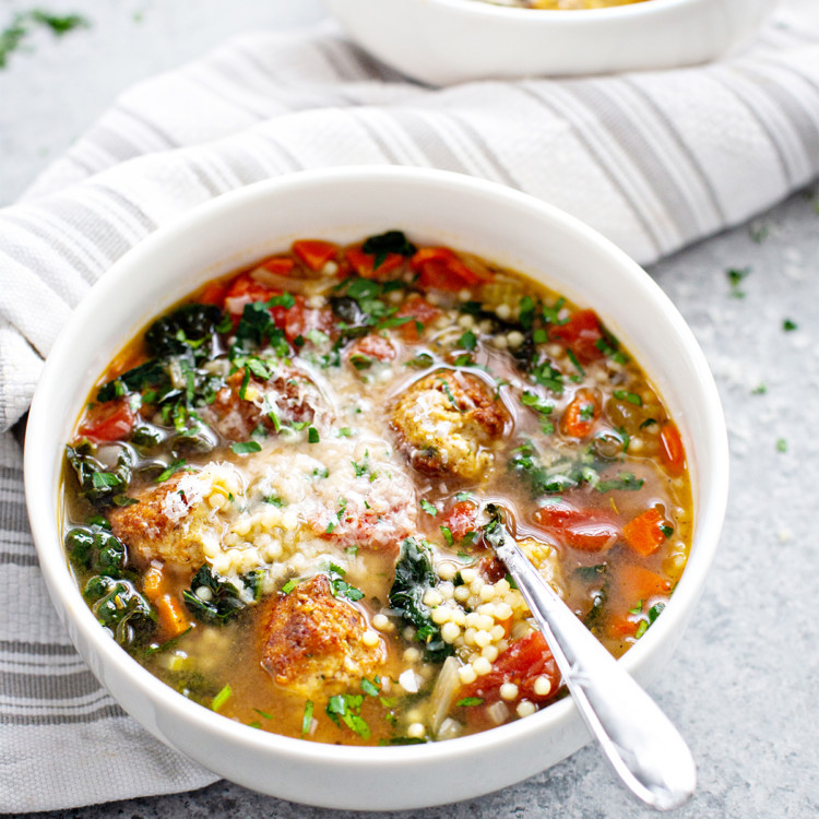 white bowl of italian wedding soup next to a cloth napkin