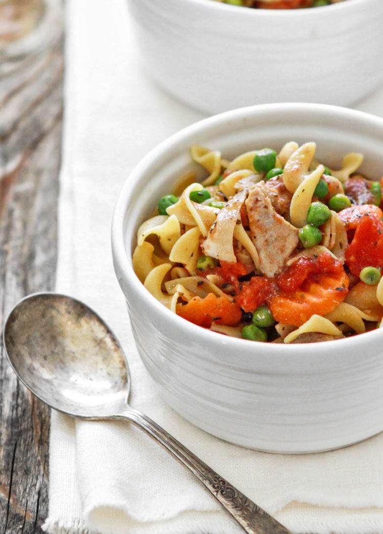 slow cooker chicken and noodles in a white bowl on a wooden table with a spoon