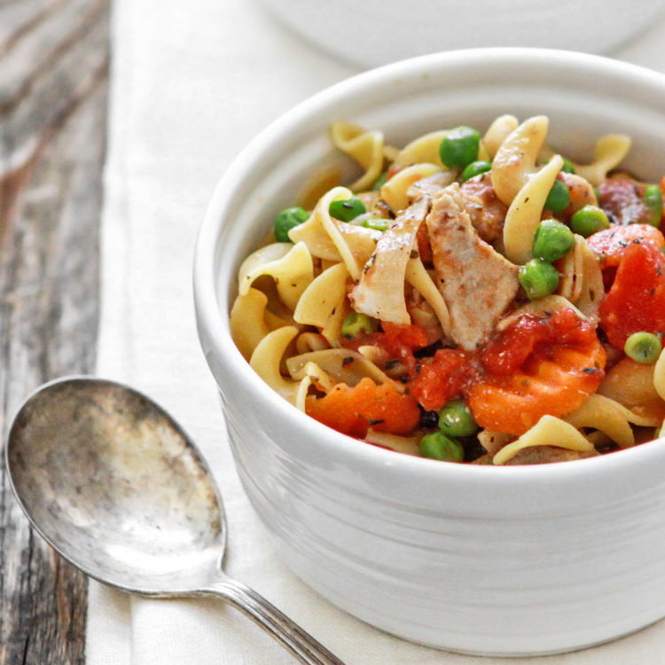 slow cooker chicken and noodles in a white bowl on a wooden table with a spoon