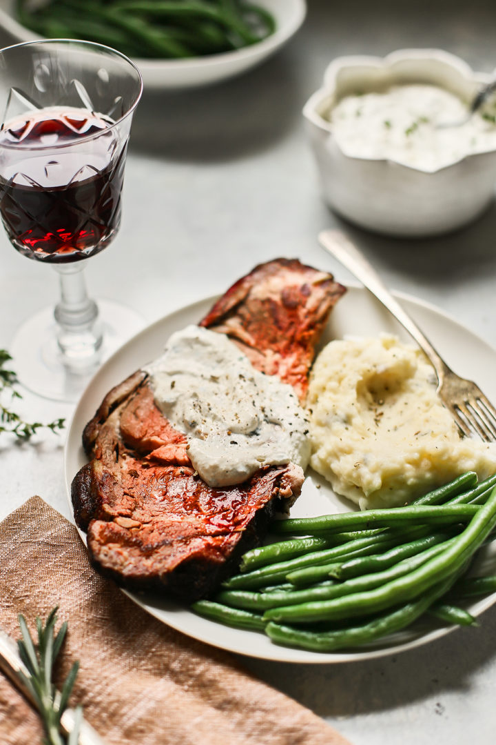 a slice of smoked prime rib on a plate with green beans and mashed potatoes