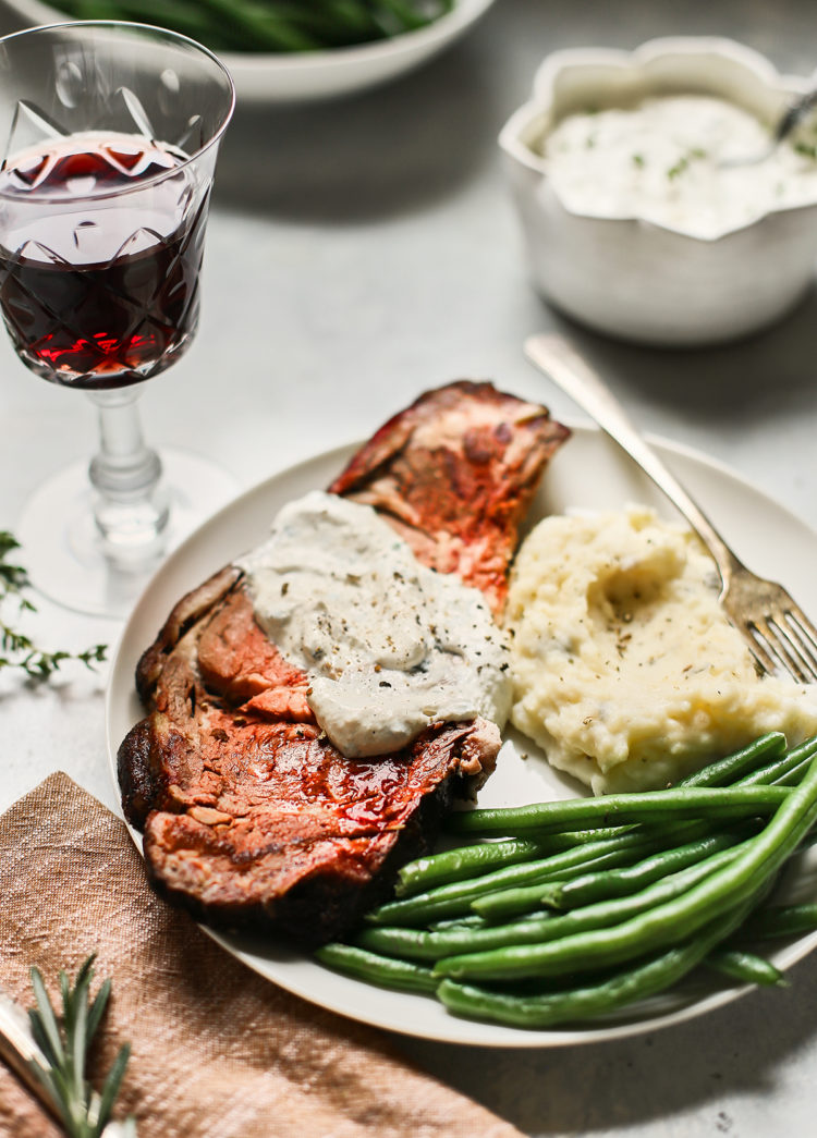 a slice of smoked prime rib on a plate with green beans and mashed potatoes