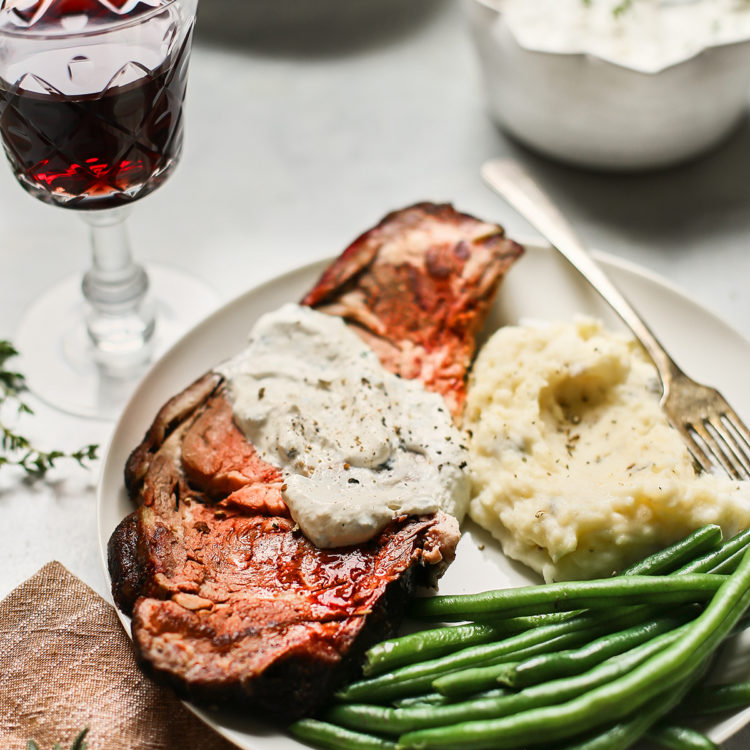 a slice of smoked prime rib on a plate with green beans and mashed potatoes