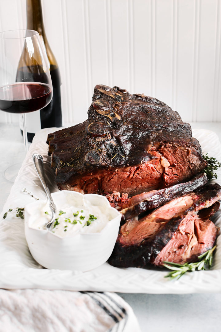 Traeger prime rib roast sliced on a white platter next to a glass of red wine