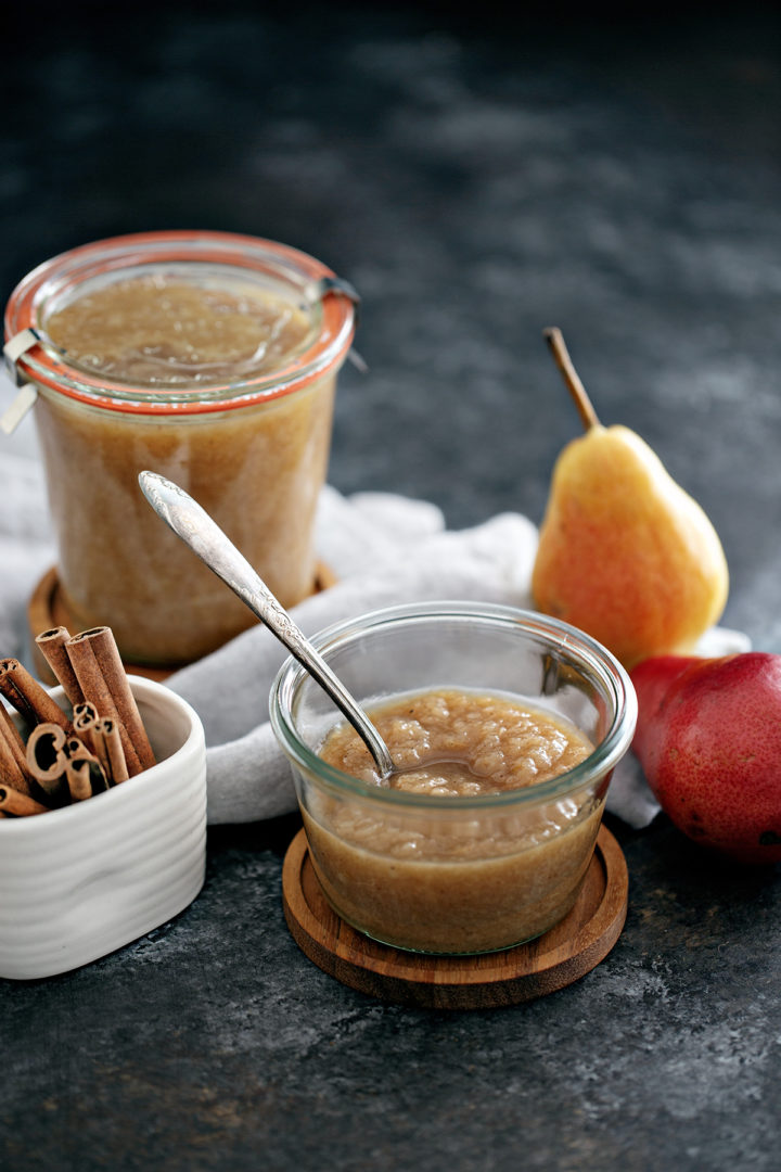 jar of homemade pear sauce with a spoon in it next to fresh pears