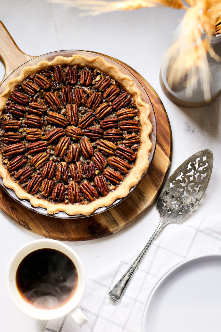 baked bourbon pecan pie on a table with a mug of hot coffee and an vintage pie server
