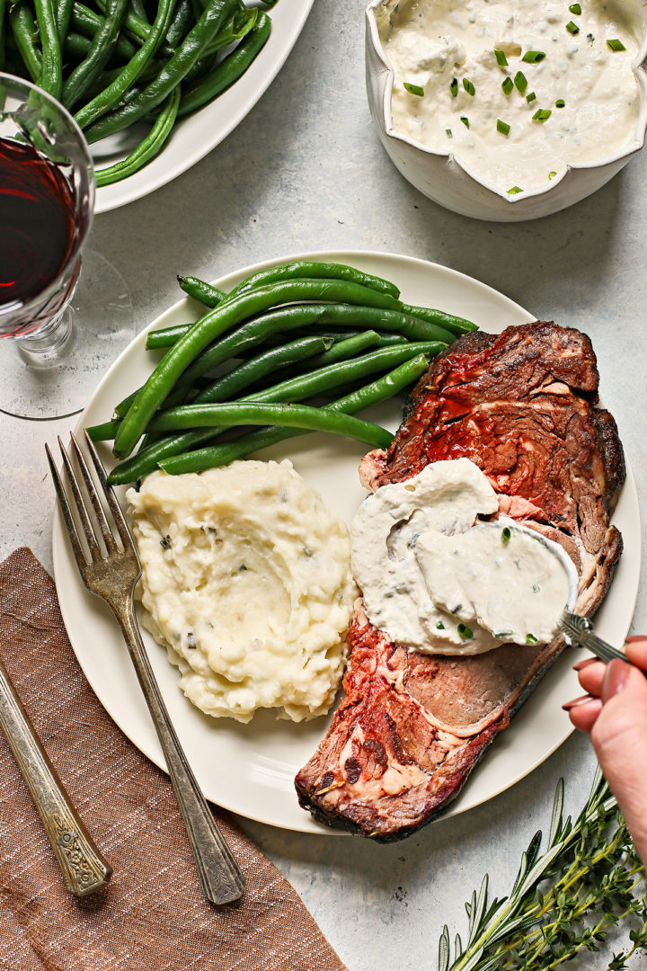 woman spreading prime rib sauce on a slice of traeger prime rib on a plate with green beans and mashed potatoes