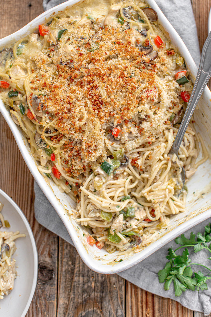 recipe for turkey tetrazzini baked in a white casserole dish on a wooden table with a serving spoon