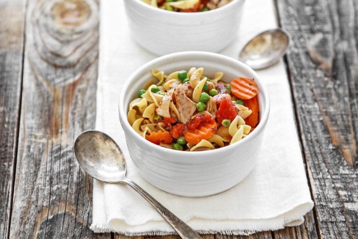 a wooden table set with bowls of chicken and noodles cooked in crock pot