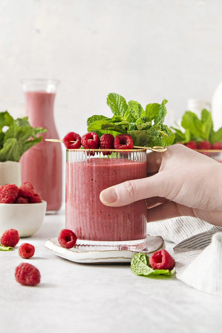 woman picking up a glass of raspberry banana smoothie