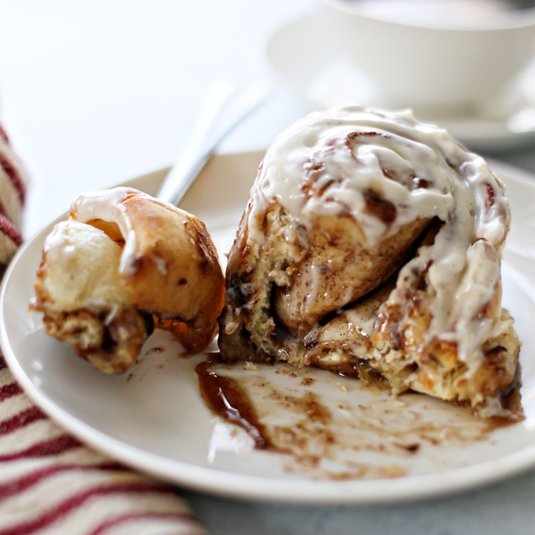 homemade cinnamon roll on a plate covered in bourbon cream cheese frosting