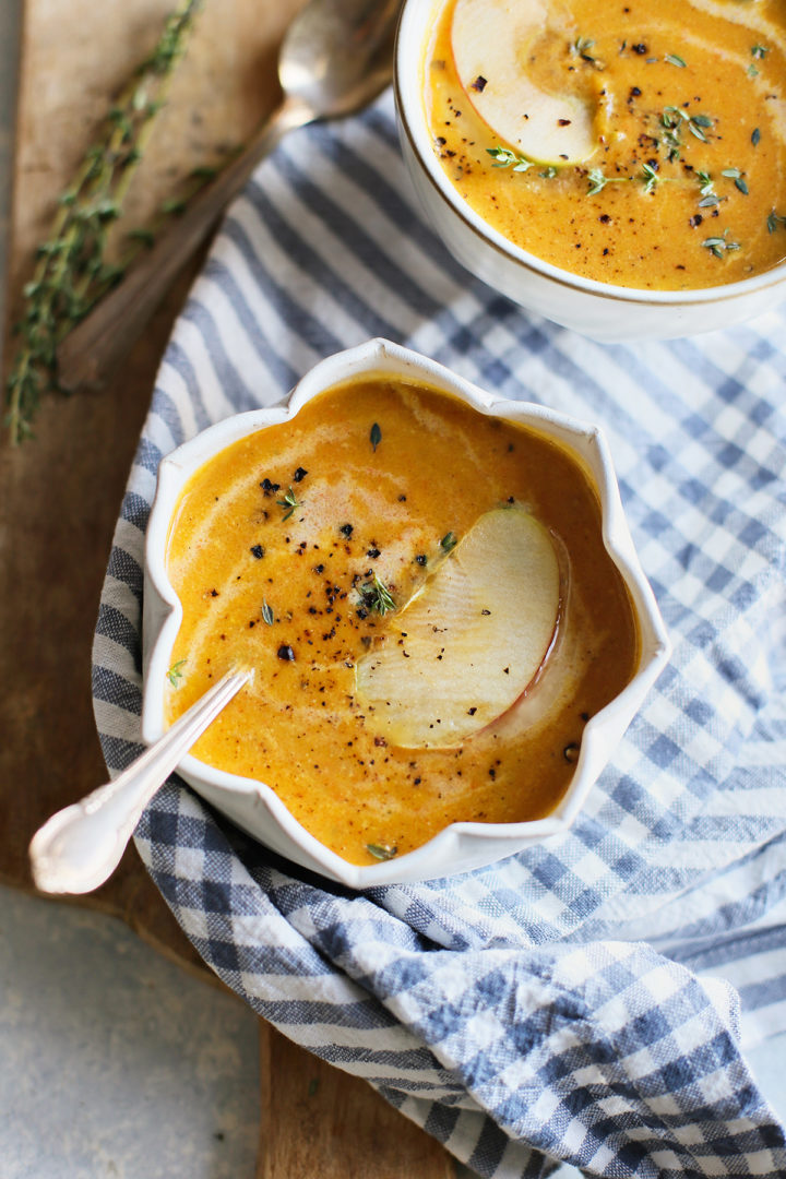 close up of a white bowl and spoon with butternut squash soup and apple	