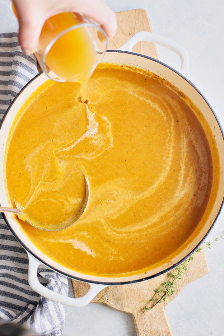 woman adding apple juice to spiced butternut soup	