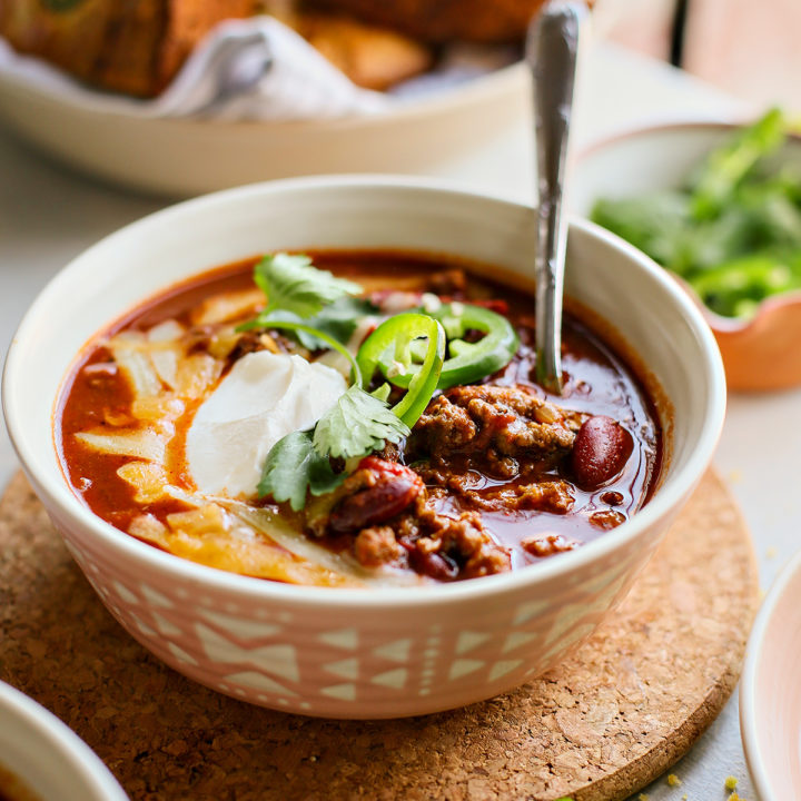 bowl of ground beef chili topped with sour cream, jalapeno, cheese, and cilantro