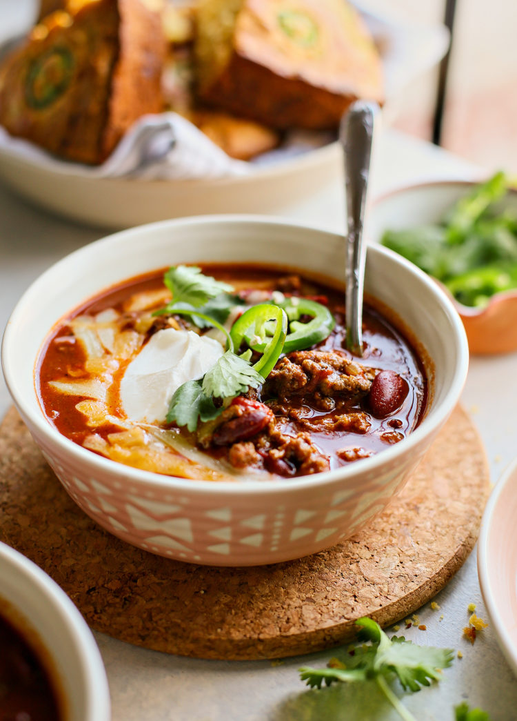 bowl of ground beef chili topped with sour cream, jalapeno, cheese, and cilantro