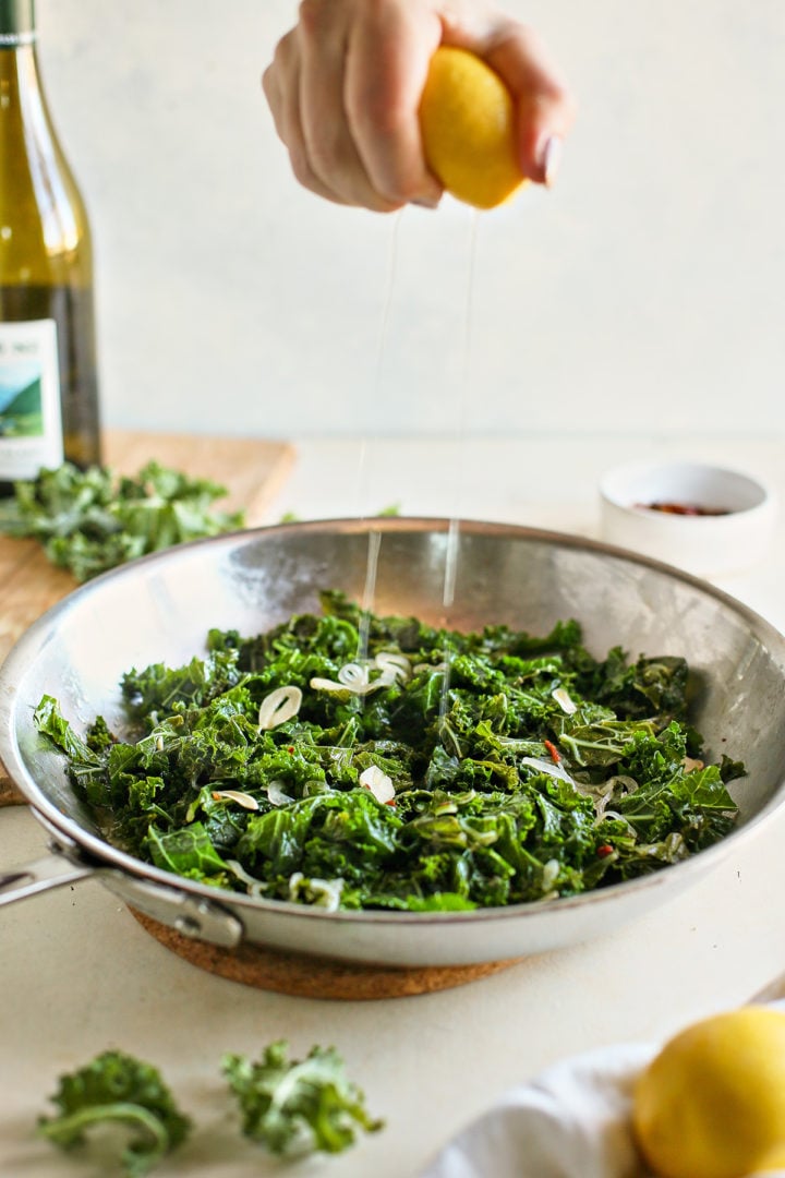 woman adding lemon juice to a pan of  sauteed kale