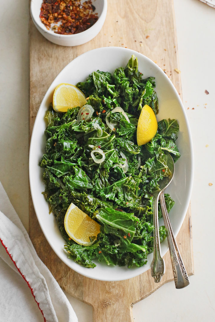 garlic sauteed kale in a white serving dish on a wooden board