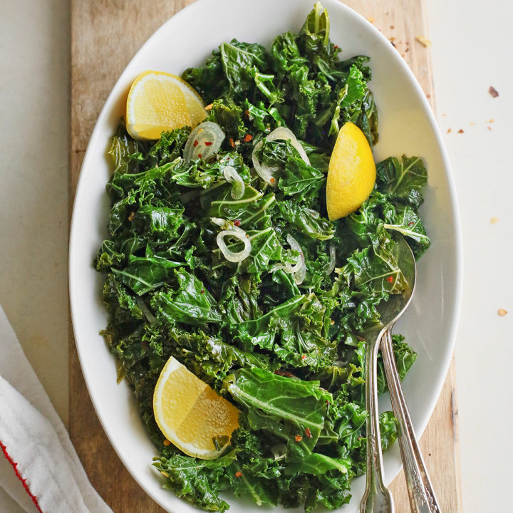 a white bowl of garlic sauteed kale on a wooden cutting board
