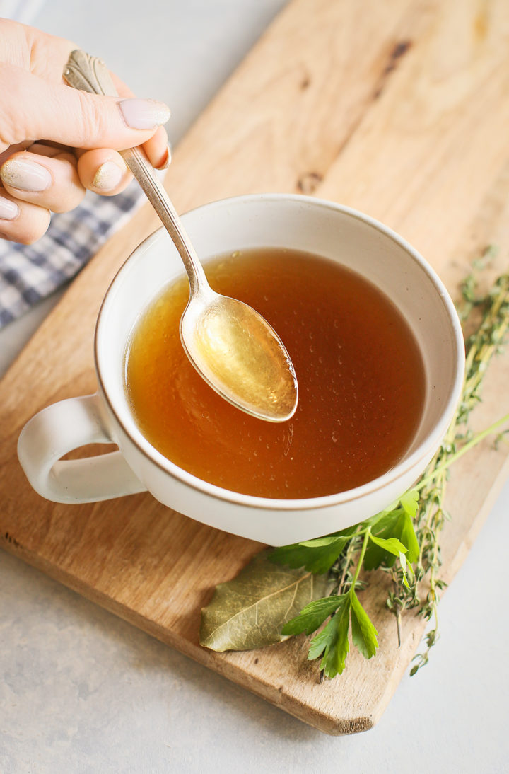 woman stirring a mug of Instant Pot chicken stock with a spoon