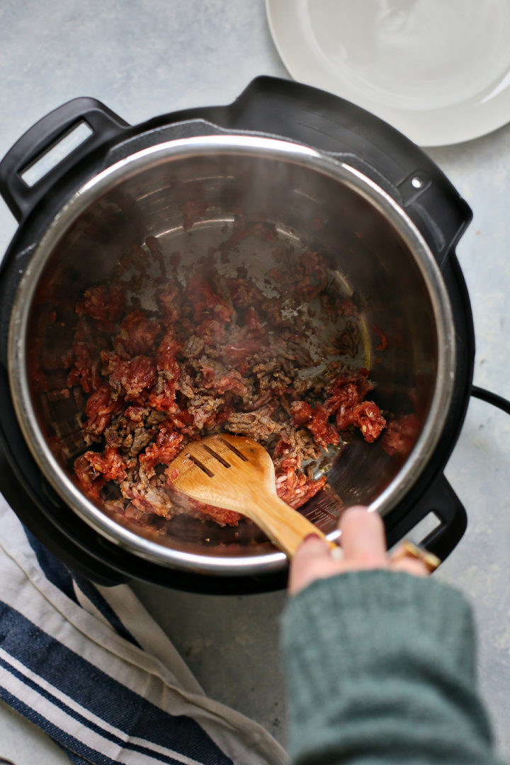 Woman browning Italian sausage in an instant pot for lentil soup