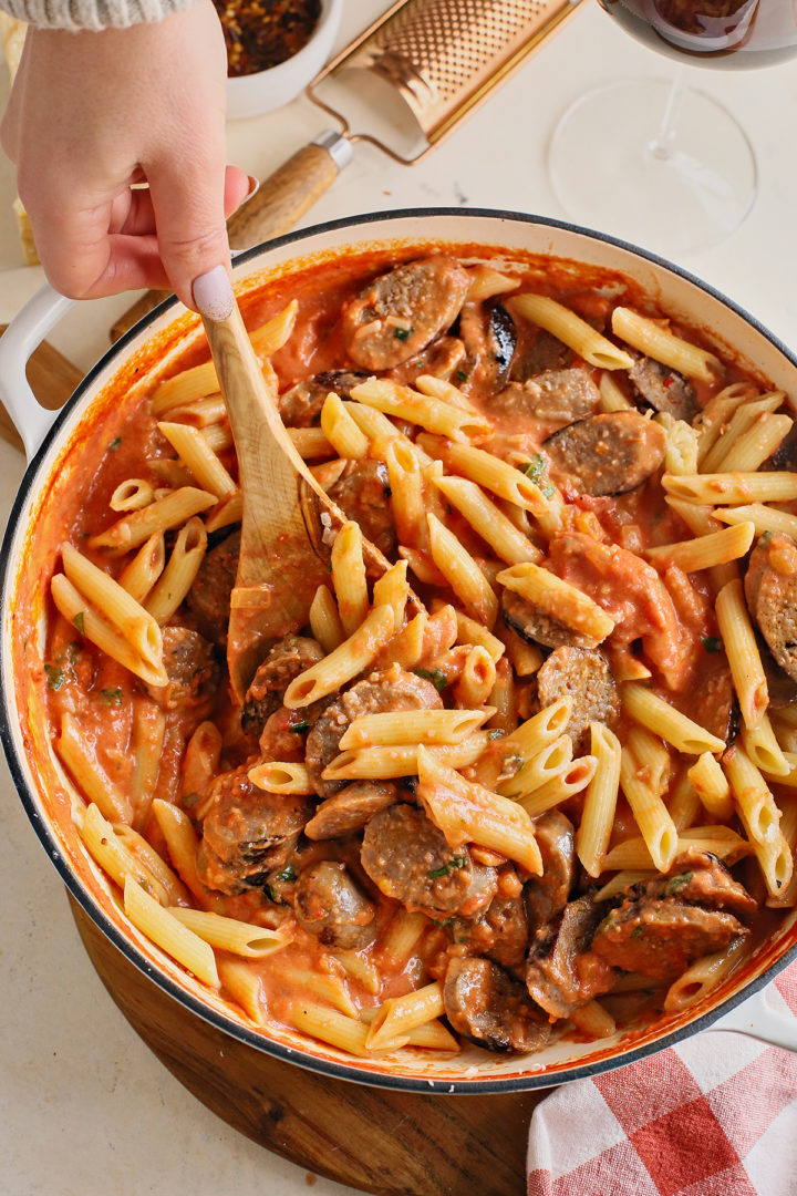 woman stirring sausage with penne with vodka sauce 
