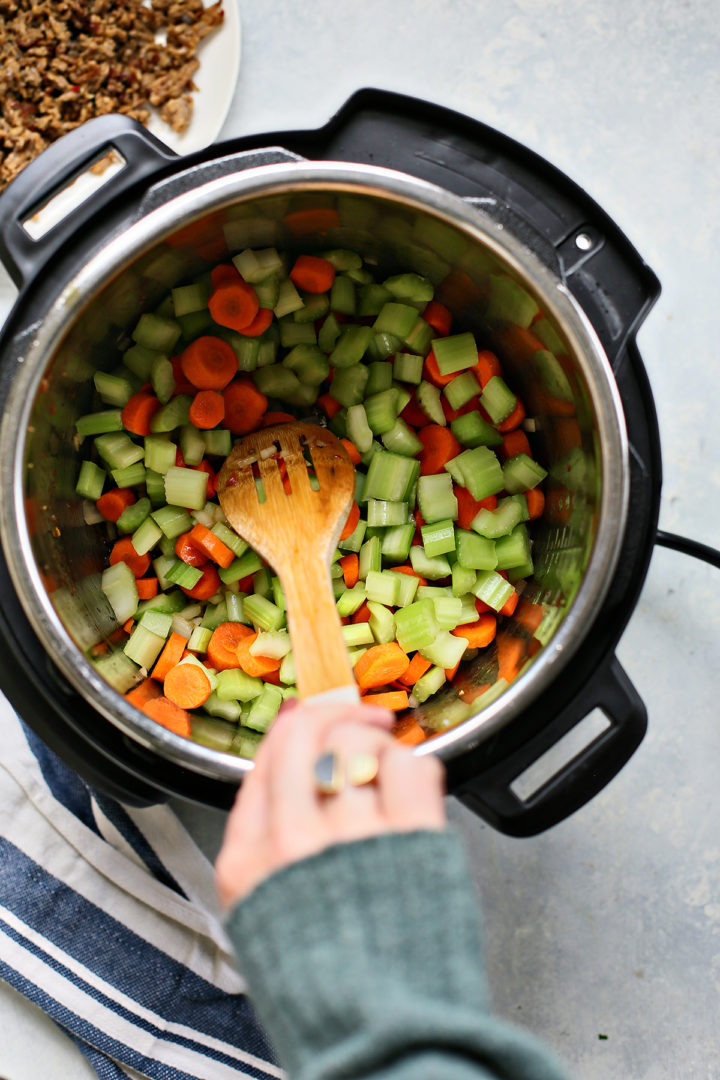 stirring carrot and celery in an instant pot to make lentil soup