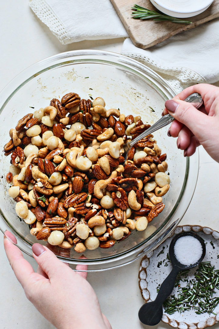 woman stirring mixed nuts with other ingredients to make roasted bar nuts