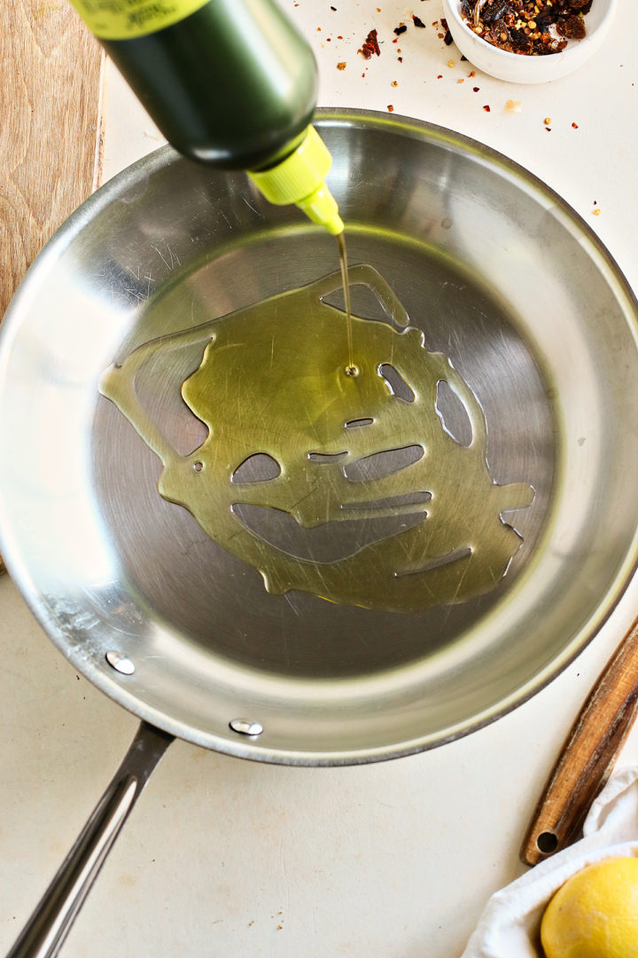 adding olive oil to a pan to make garlic sauteed kale