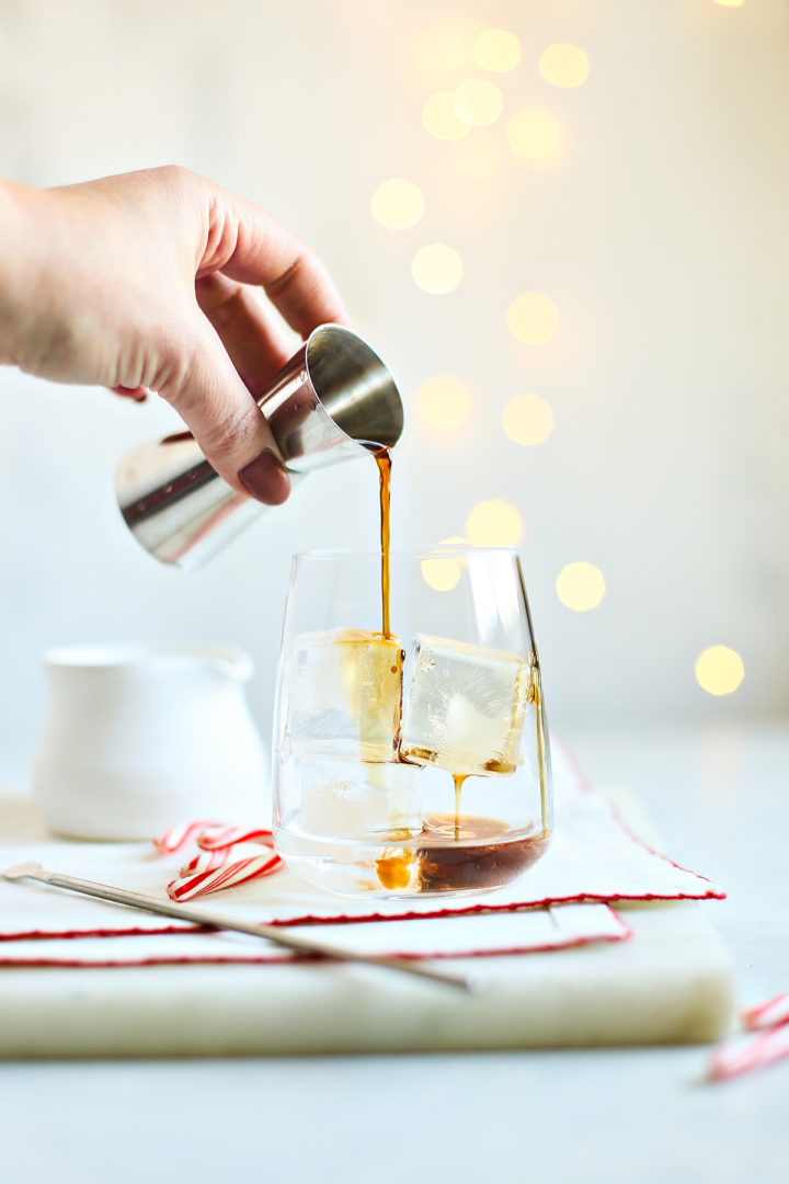 adding coffee liqueur to a glass to make a Christmas white Russian